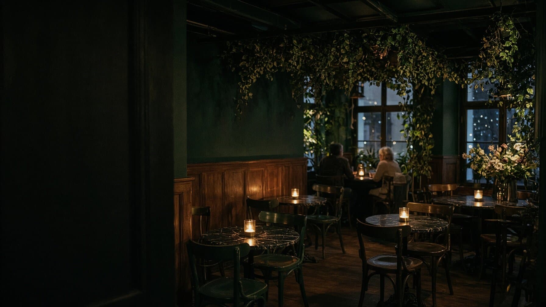 The dining room at night: bentwood chairs, small marble tables, candles on every table, greenery and flowers hung through the room.