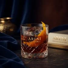An old fashioned in cut crystal, one large cube and a twist of orange